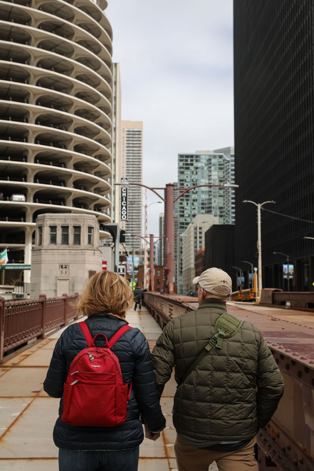 Couple walking hand-in-hand on a bridge in Chicago with Marina City and skyscrapers in the background.