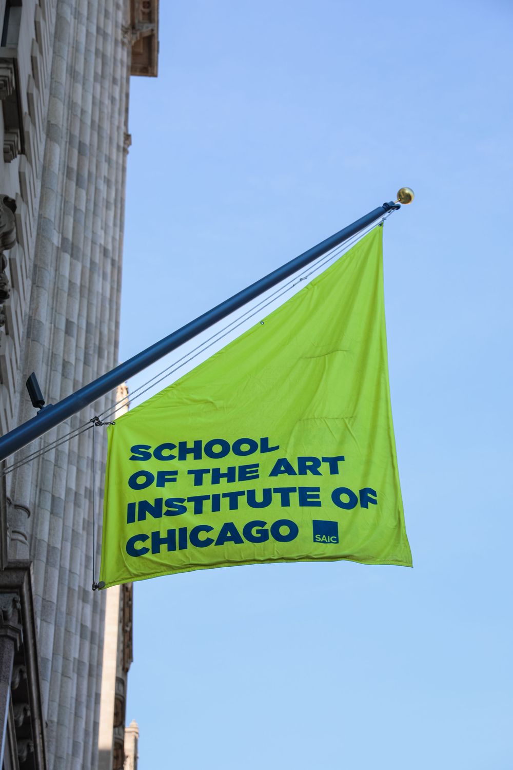 Bright green flag for the School of the Art Institute of Chicago mounted on a pole against a blue sky.