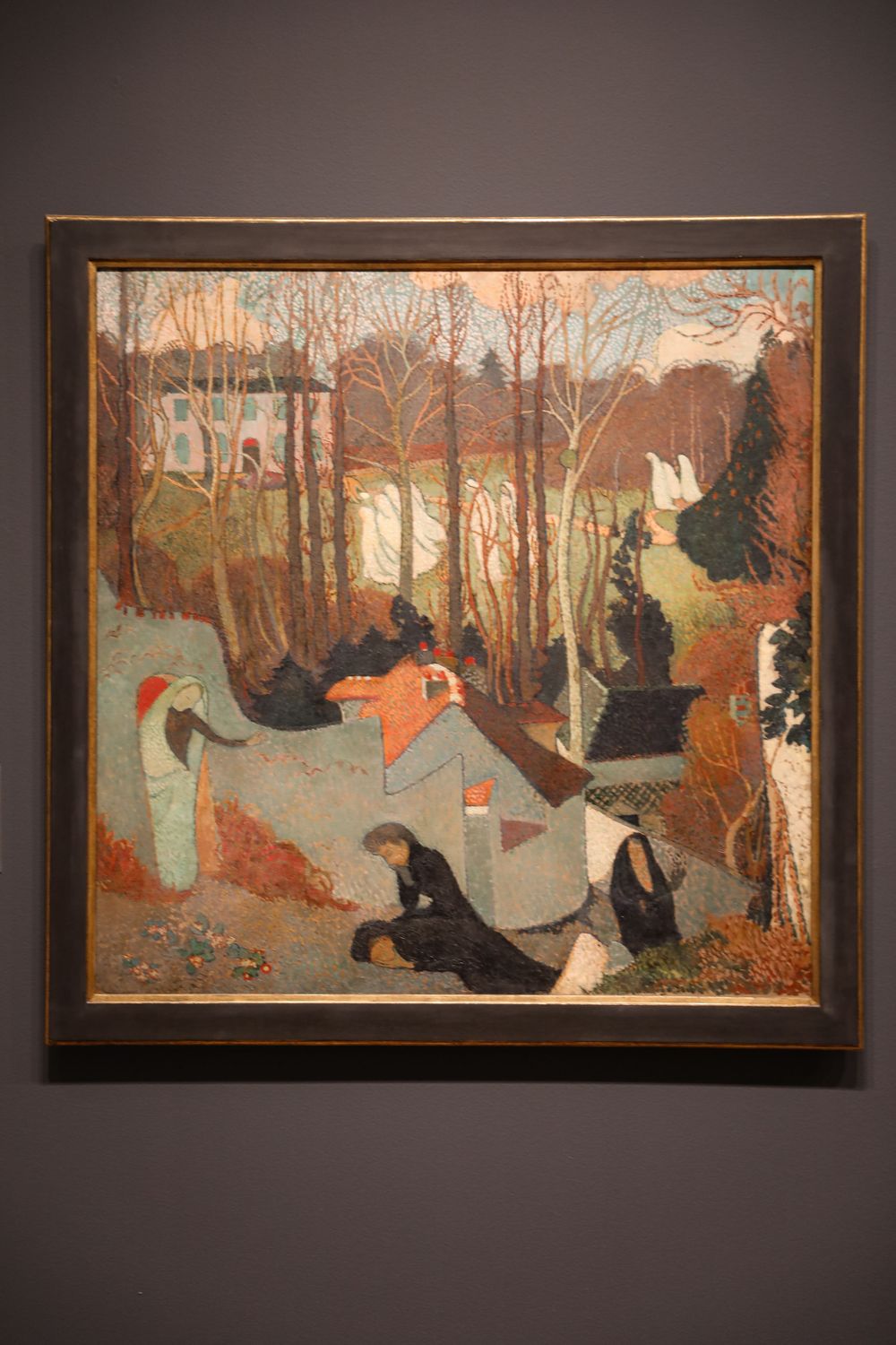 Post-Impressionist painting displayed in museum showing figures in a garden landscape with bare trees and a white building.