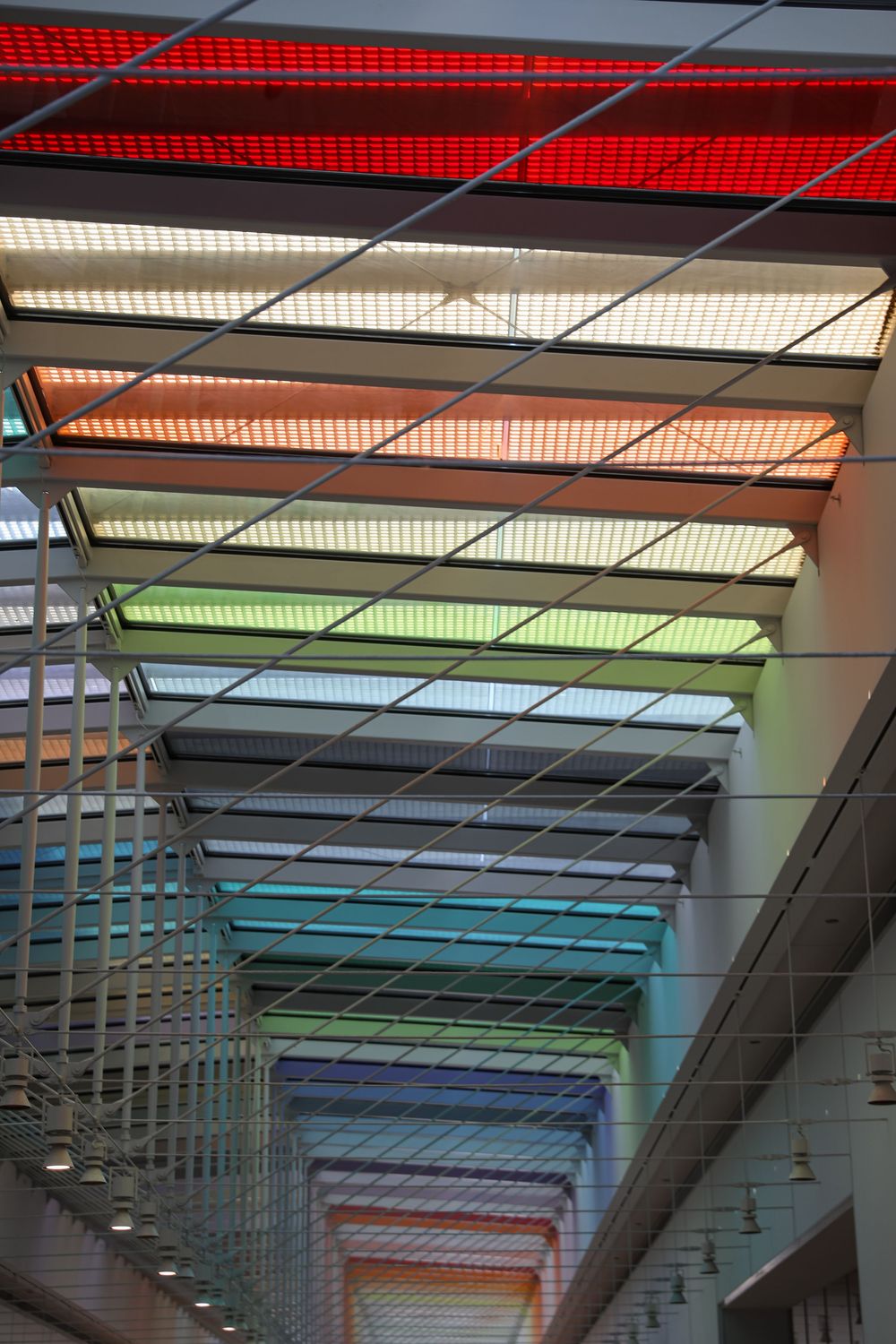 Rainbow colored illuminated ceiling panels in a modern building atrium creating a vibrant spectrum of light.