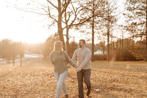 Couple holding hands and smiling at each other in a sunlit autumn park with golden trees.