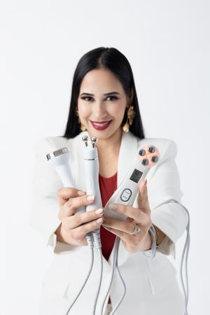 Beauty professional displaying skincare devices while wearing white blazer and red top.