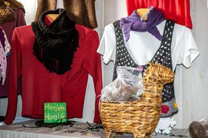 Handmade knit scarves displayed on mannequins beside a wicker basket at a craft fair vendor booth.