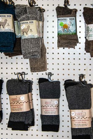 Alpaca wool outdoor adventure socks displayed on pegboard, including survival and backpacking styles in gray and dark tones.