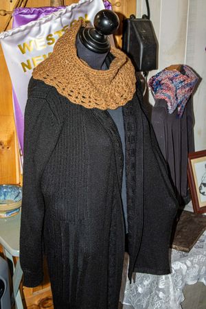 Black knit cardigan on mannequin with brown crochet cowl scarf and colorful knit accessory displayed indoors.