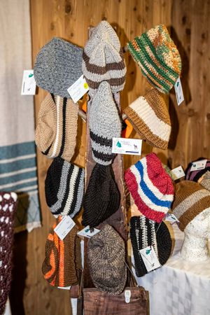 Colorful handknitted wool hats displayed on a wooden rack at a craft market, featuring striped patterns in various colors.