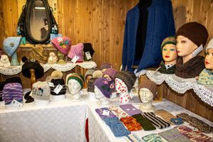 Handmade knitted hats and accessories displayed on mannequin heads at a craft market stall with wooden walls.