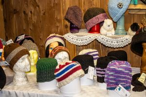 Colorful handknitted winter hats displayed on white mannequin heads at a craft market stall with wooden walls.