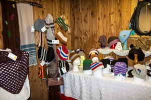 Colorful handmade knitted hats and accessories displayed on mannequin heads on a white table in a cozy wooden shop.