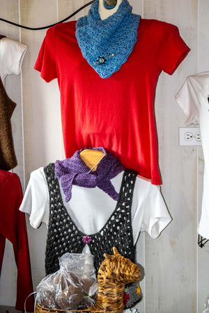 Handmade crochet scarves displayed on mannequins with red and white shirts at a craft market.