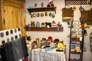 Cozy craft shop display with knitted hats, handmade ornaments on shelves, woven blanket, and colorful accessories on a decorated table.