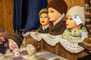 Mannequin heads displaying colorful knitted hats, scarves, and winter accessories at a craft market stall.