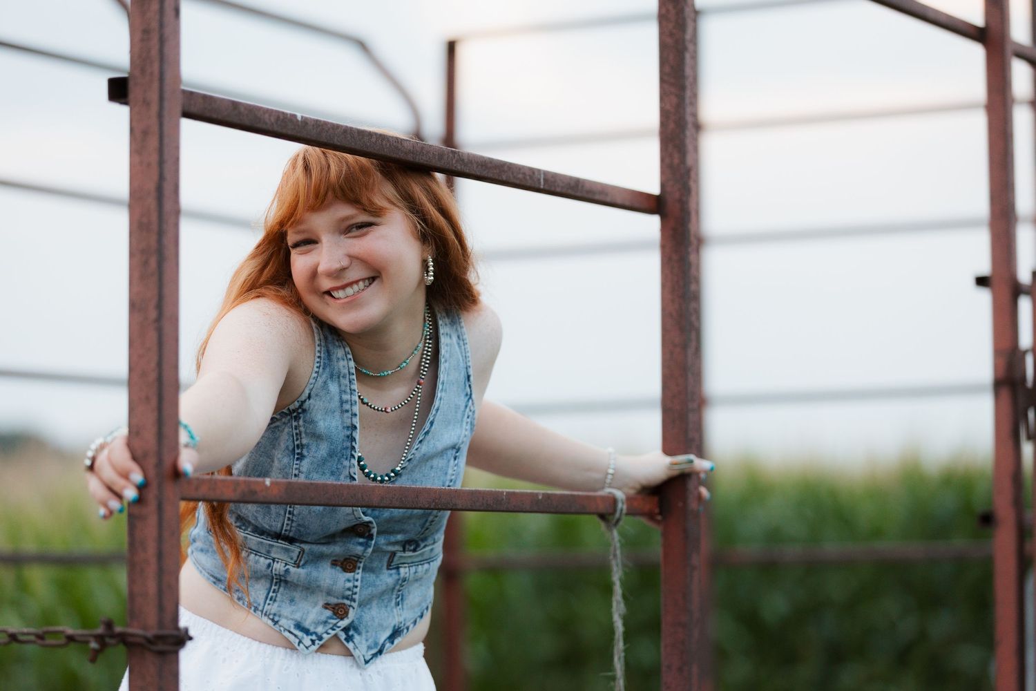 Woman smiling among vintage red tractors and farm equipment in a rural junkyard setting.