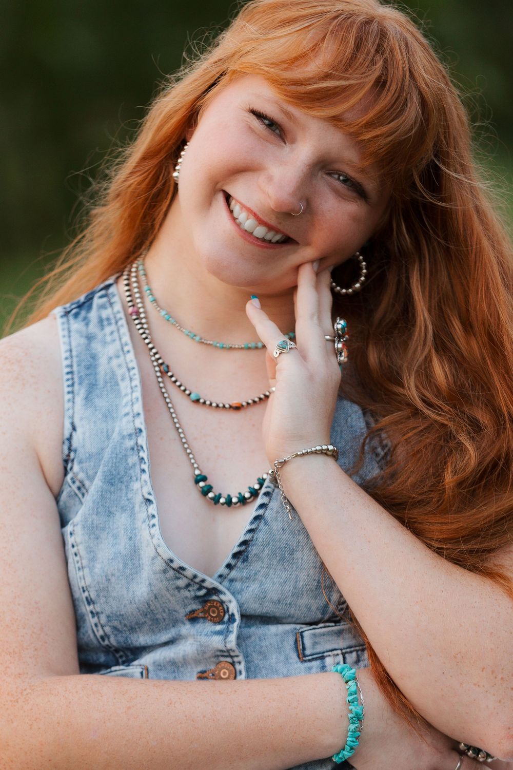 Smiling redhead woman wearing turquoise jewelry and denim vest outdoors.