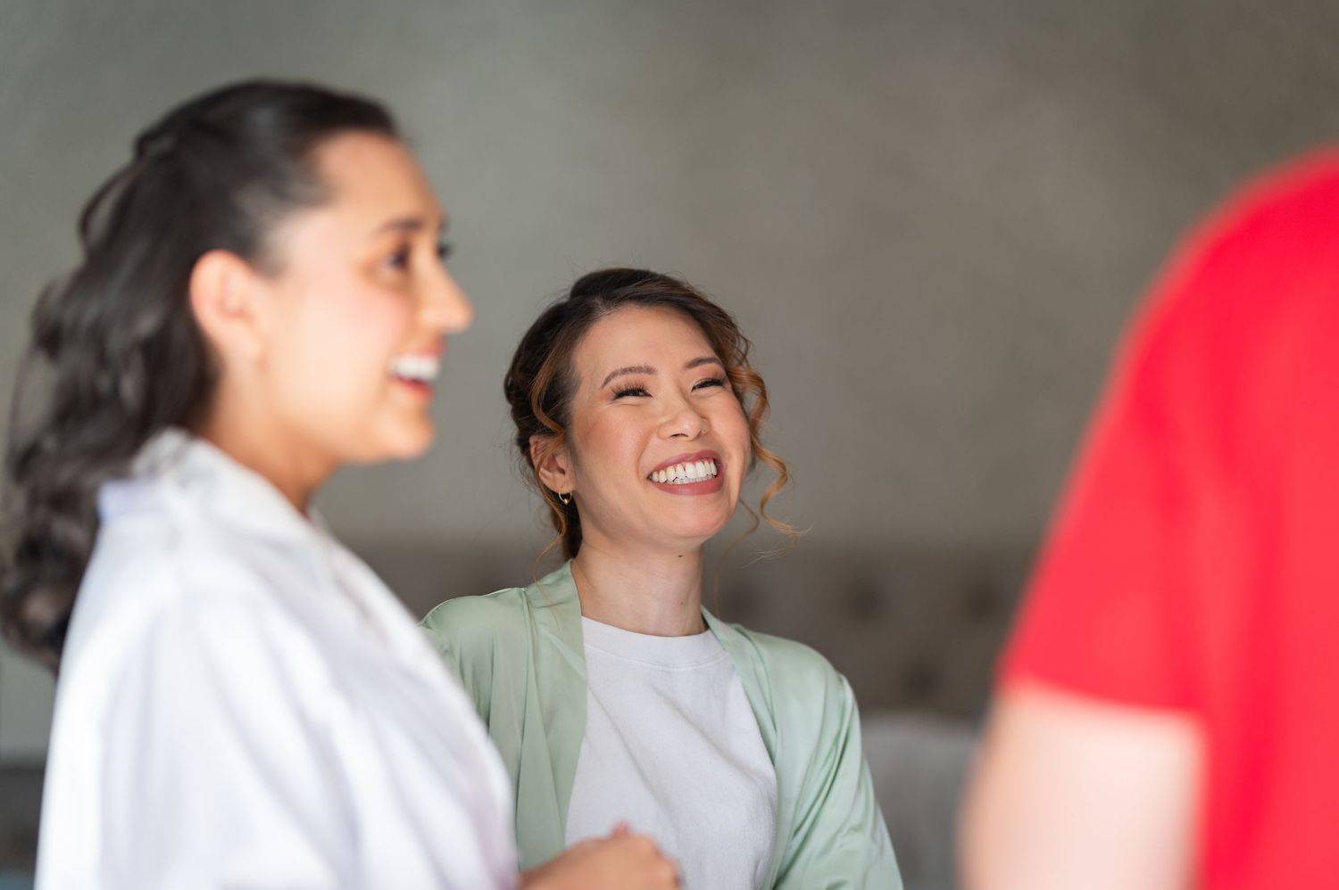 Two women smiling and laughing together in a casual indoor setting, wearing white and green outfits.
