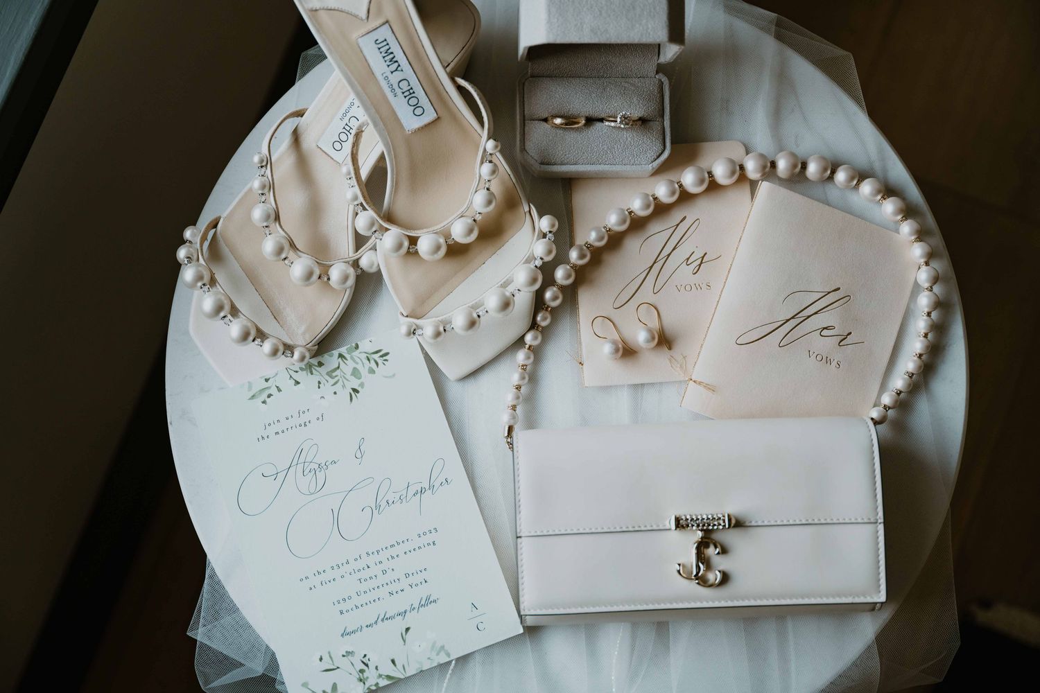 Elegant bridal flat lay featuring pearl jewelry, Jimmy Choo heels, rings, and wedding stationery.