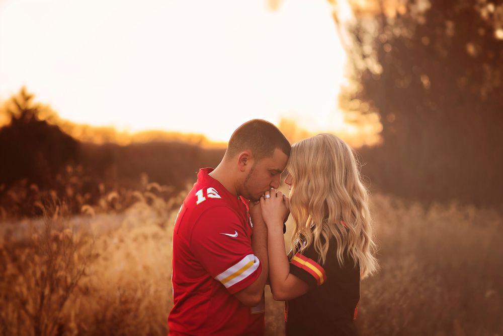 Couple sharing a romantic moment at golden sunset in a field, man in red jersey holding womans hands tenderly.