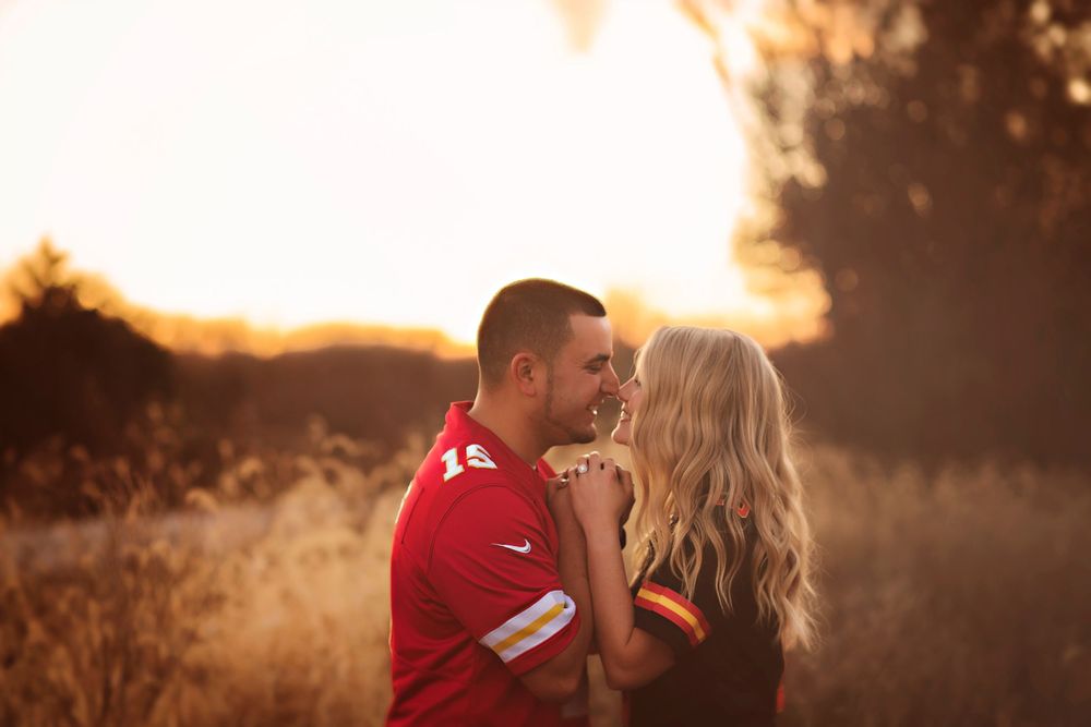 Couple sharing a romantic moment at golden hour in a field, man in red jersey and woman with long blonde hair.
