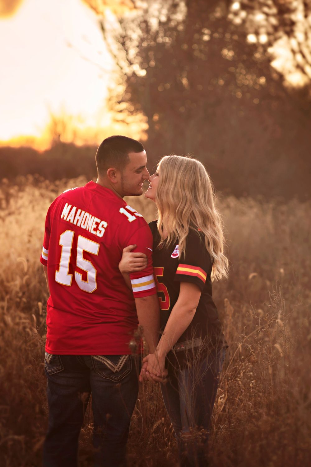 Couple kissing in golden field at sunset wearing Kansas City Chiefs Mahomes jerseys, romantic engagement photo.
