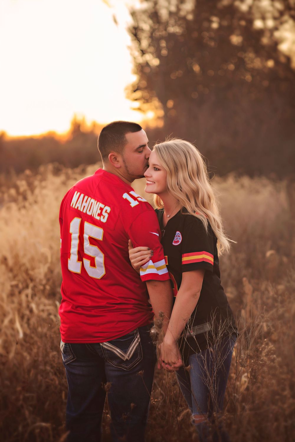 Couple sharing a kiss in a golden field at sunset, wearing Kansas City Chiefs jerseys number 15.