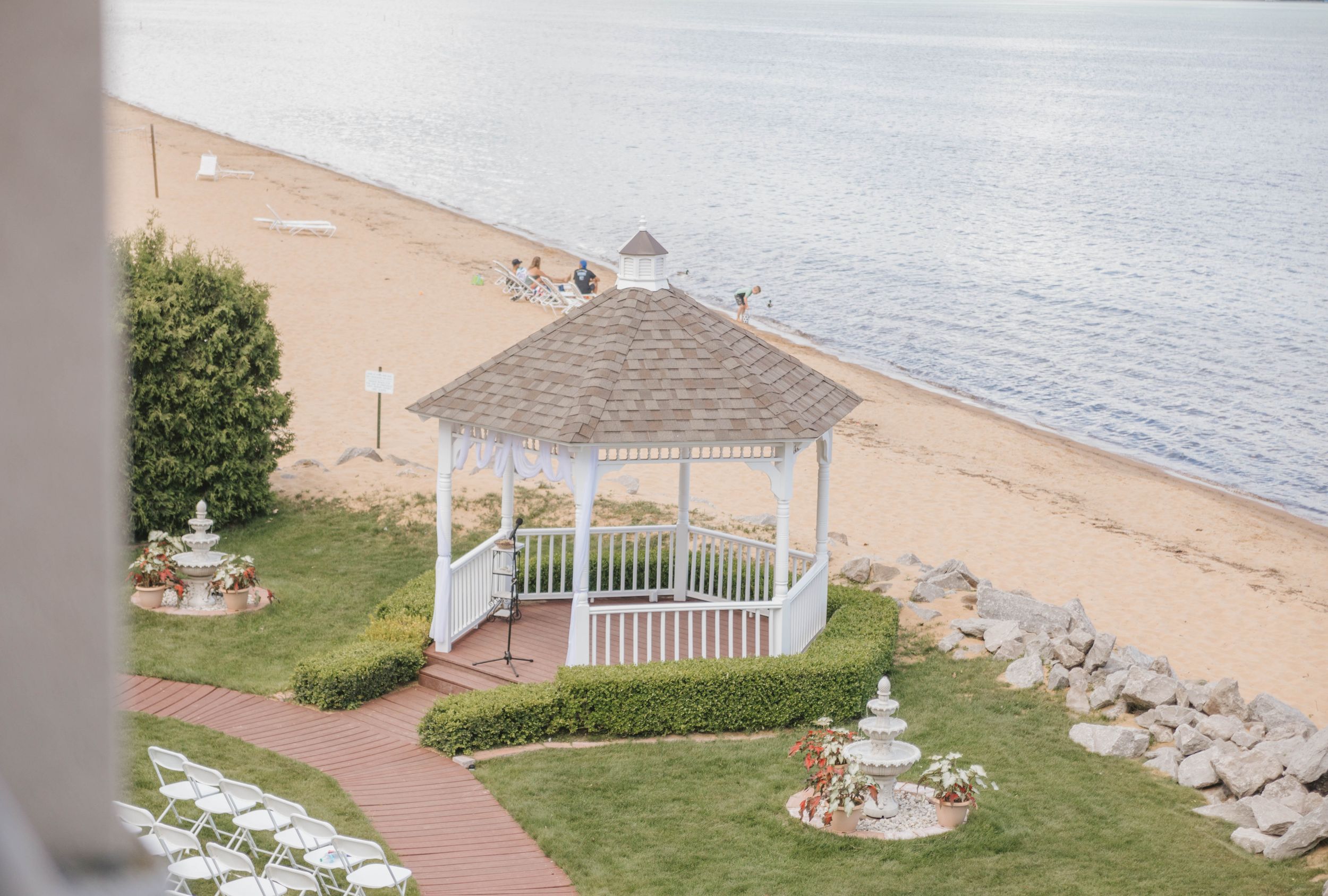 White gazebo on a beachfront lawn with fountain, white chairs, and ocean views at a waterfront wedding venue.