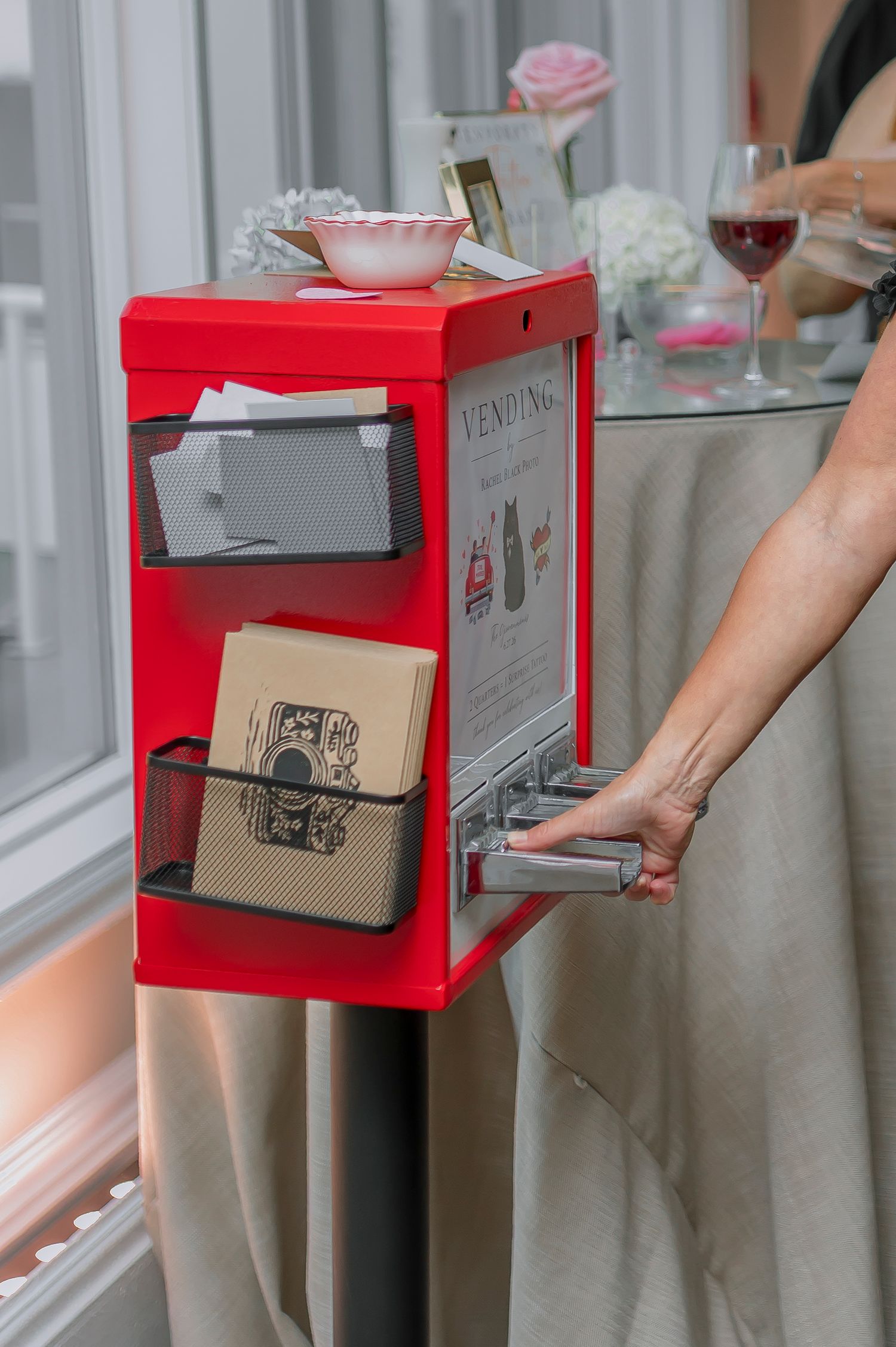 A red vending machine with mesh pockets holding cards and notebooks at an elegant event with wine glasses.