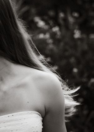 Black and white photo of a young woman with long hair wearing a white strapless dress outdoors.