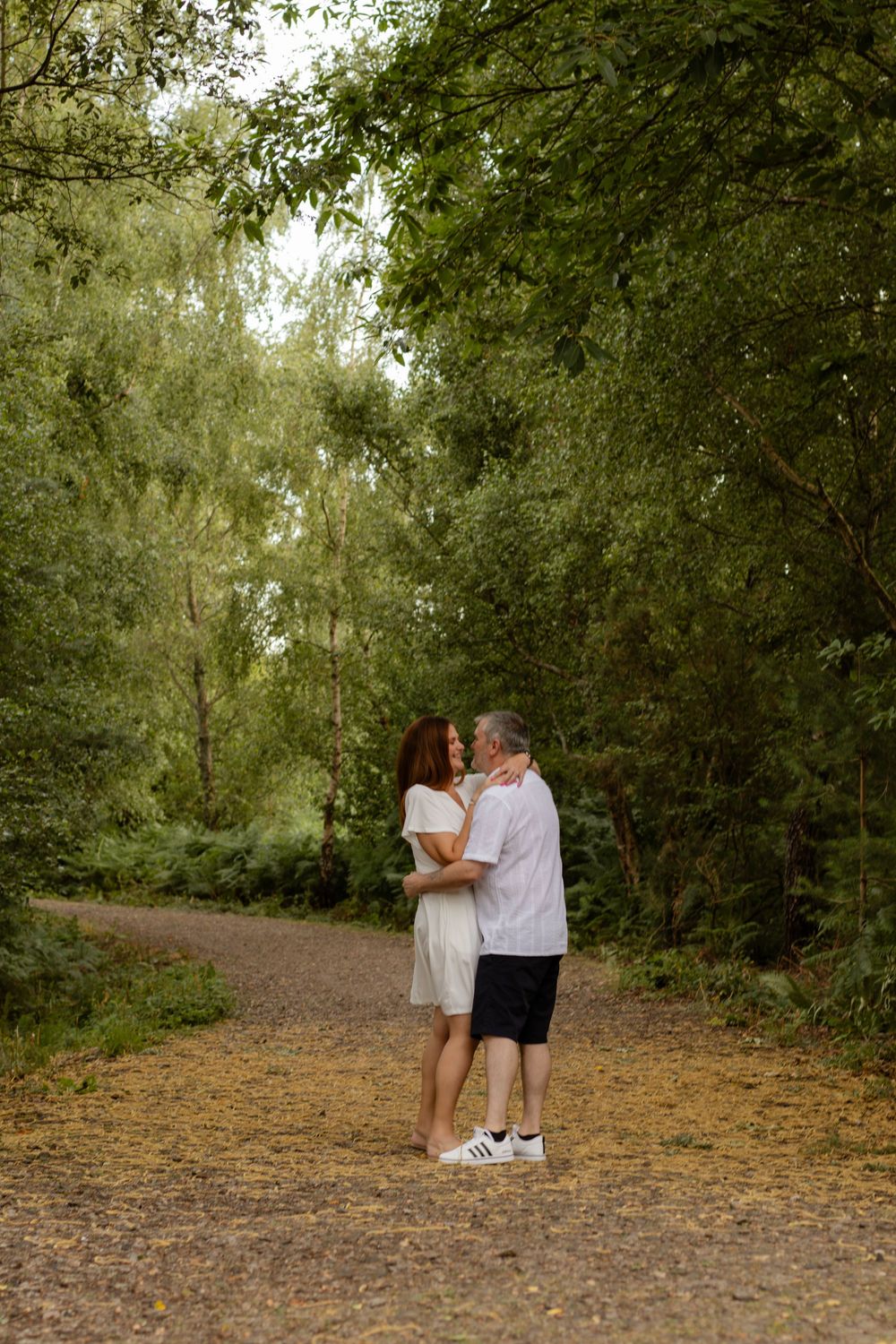 Couple embracing on a forest path surrounded by lush green trees.