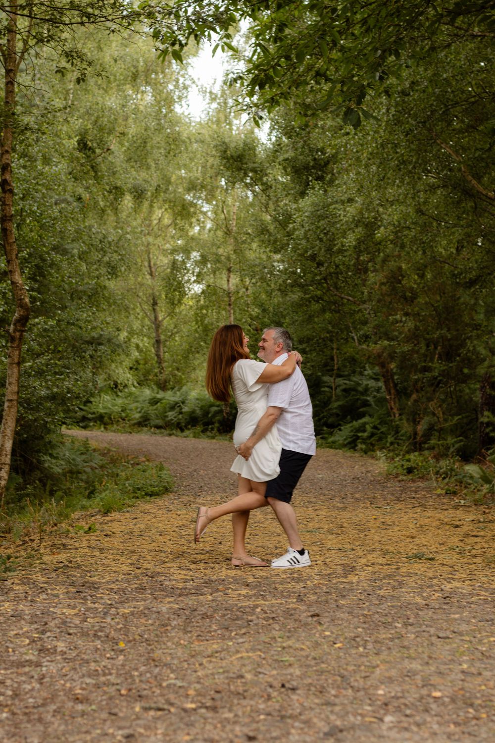 Man lifting woman in a joyful embrace on a woodland trail.