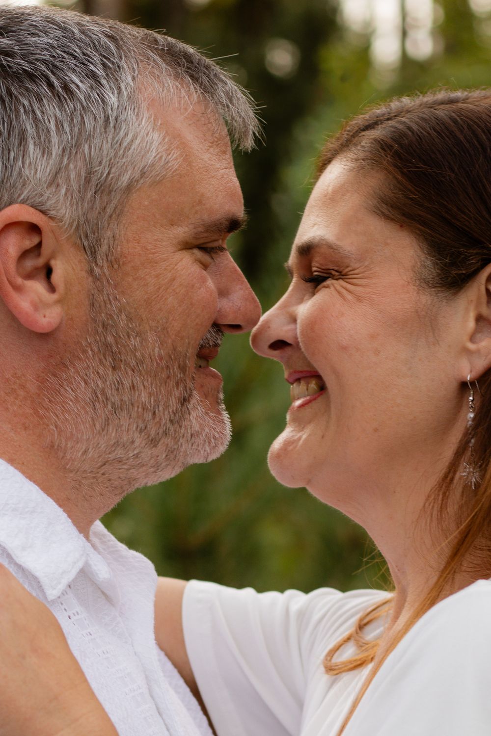 Middle-aged couple sharing a romantic moment, smiling and facing each other closely outdoors.