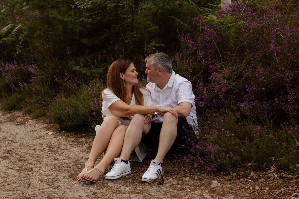 Couple sitting together on a log surrounded by purple wildflowers in a natural forest setting.