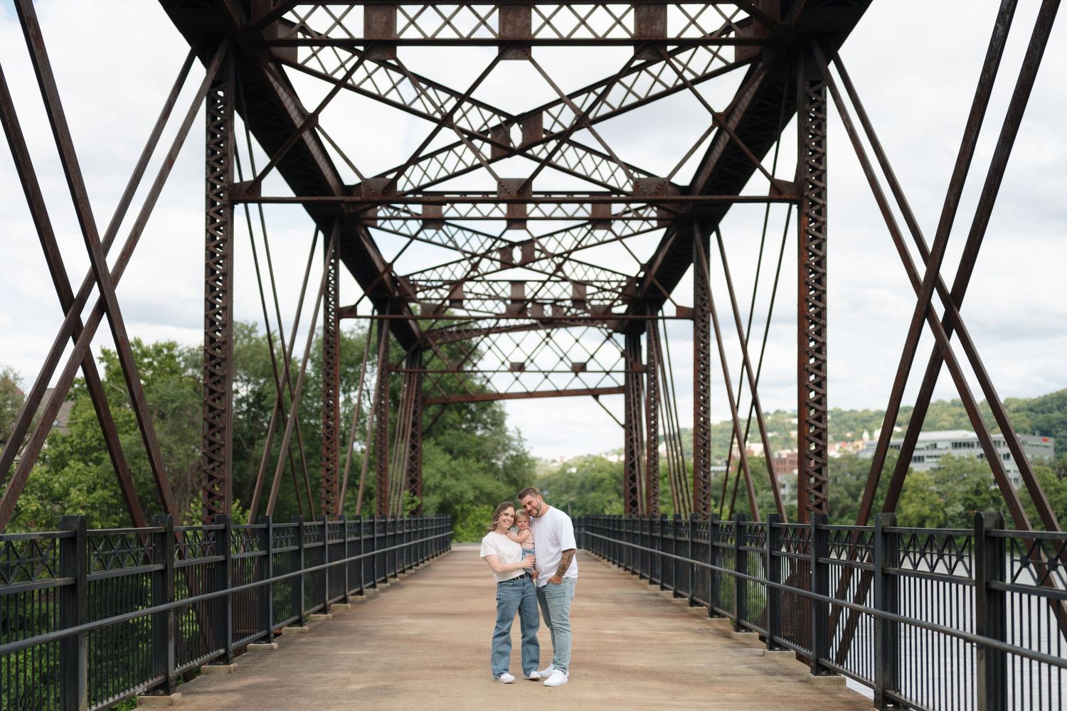 Couple sharing a tender moment on a rustic iron truss bridge walkway.