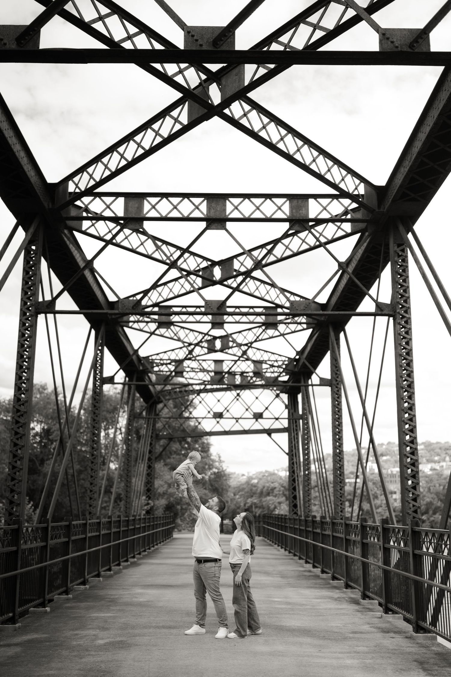Couple standing together on a vintage iron truss bridge in black and white photography.