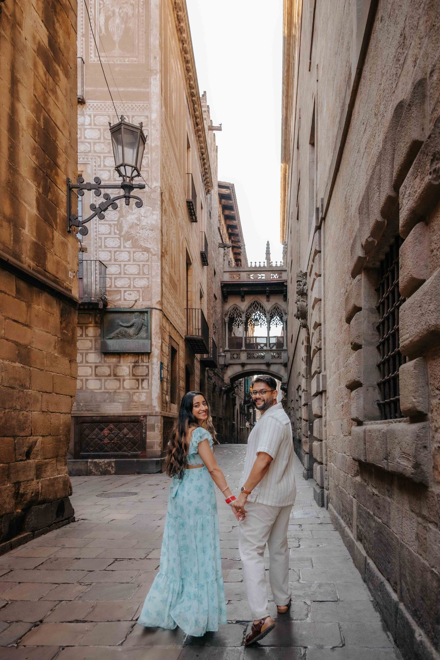 A joyful couple celebrating their anniversary walking hand-in-hand through the narrow, sunlit cobblestone streets of the Gothic Quarter