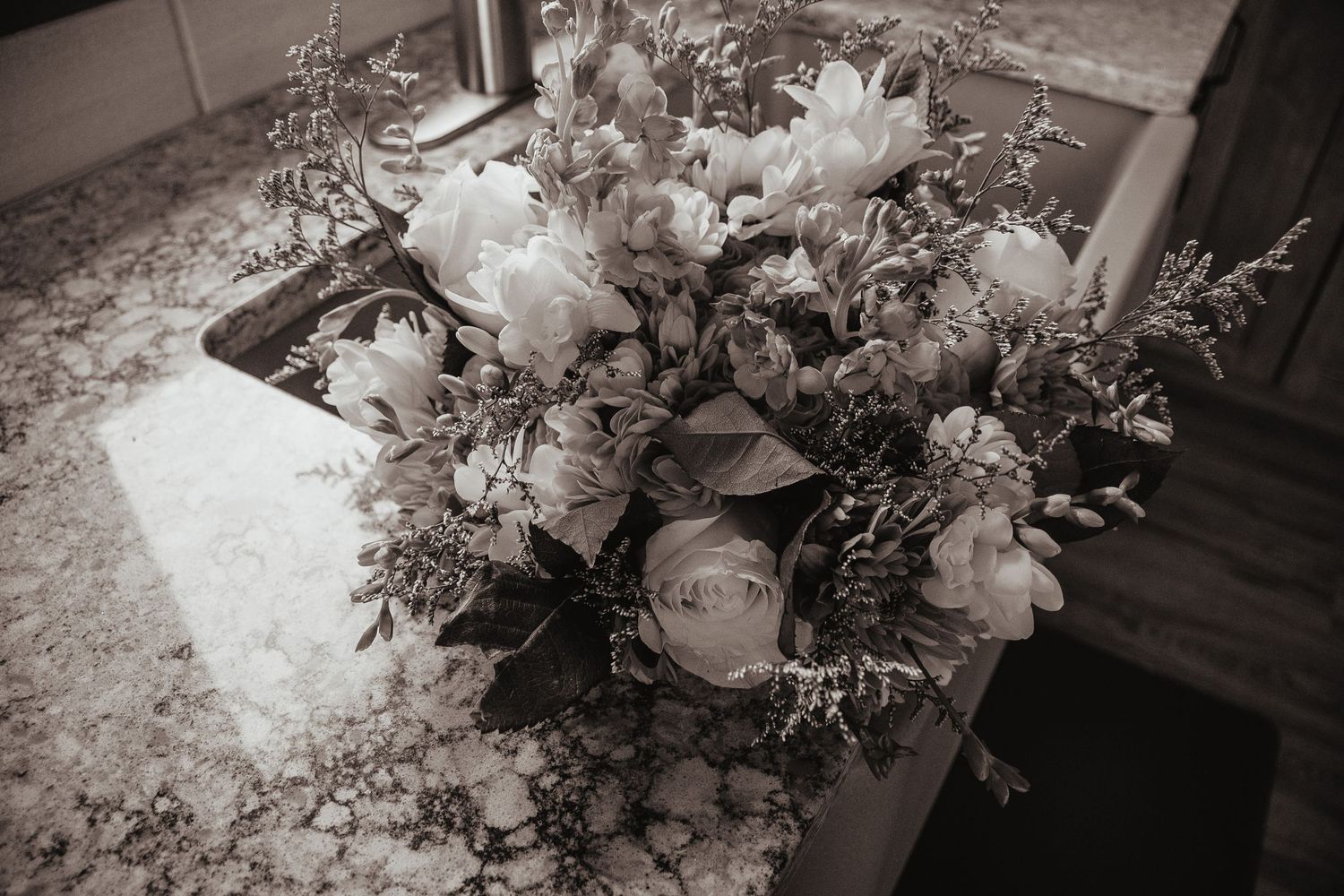 Black and white photo of a lush floral arrangement with peonies and greenery on a marble countertop.
