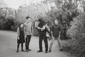 Black and white family portrait of five people laughing and playing together on a dirt path surrounded by desert trees.