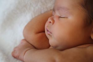 Close-up of a peaceful newborn baby sleeping on a soft white blanket with tiny hands tucked near the chin.