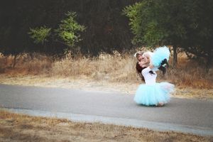 A woman in a turquoise tutu and white top lifts and hugs a little girl in a matching tutu on a quiet country road.