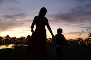 Silhouette of a mother holding her young son's hand at dusk, with a pink and purple sky and glowing lights in the background.