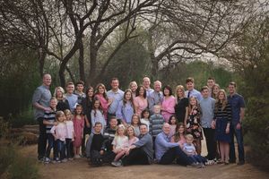 Large multi-generational family poses together outdoors among desert trees, with children seated in front and adults standing behind.