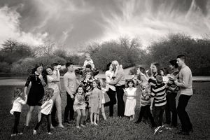 Black and white photo of a large extended family gathered together in a grassy field under a dramatic cloudy sky.