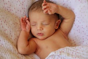 Newborn baby sleeping peacefully on a soft pink-dotted blanket with tiny hands raised near the face.