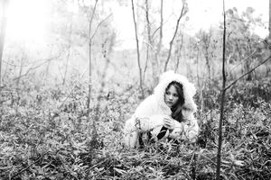 Black and white portrait of a girl in a white fur-trimmed hooded coat sitting in a misty autumn forest.