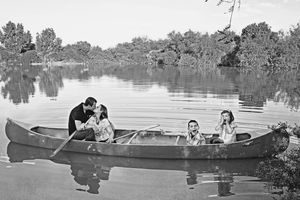 A black and white photo of two couples sharing a canoe on a calm lake, one pair kissing and the other smiling.