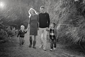 Black and white family portrait of parents and two young sons walking hand in hand along an outdoor path.
