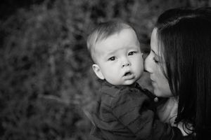 Black and white photo of a mother holding her baby boy close as he looks curiously at the camera.