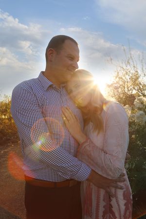 Smiling couple embracing outdoors at sunset, with warm sun flare glowing between them.