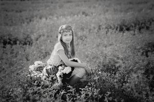 Black and white portrait of a young girl in a floral headband sitting in a grassy field.