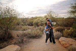 Father carrying a boy on his shoulders while hugging a woman and baby on a desert nature trail.
