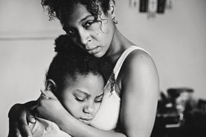 Black and white portrait of a mother holding her daughter in a tight, loving embrace while the child rests her head on her shoulder.